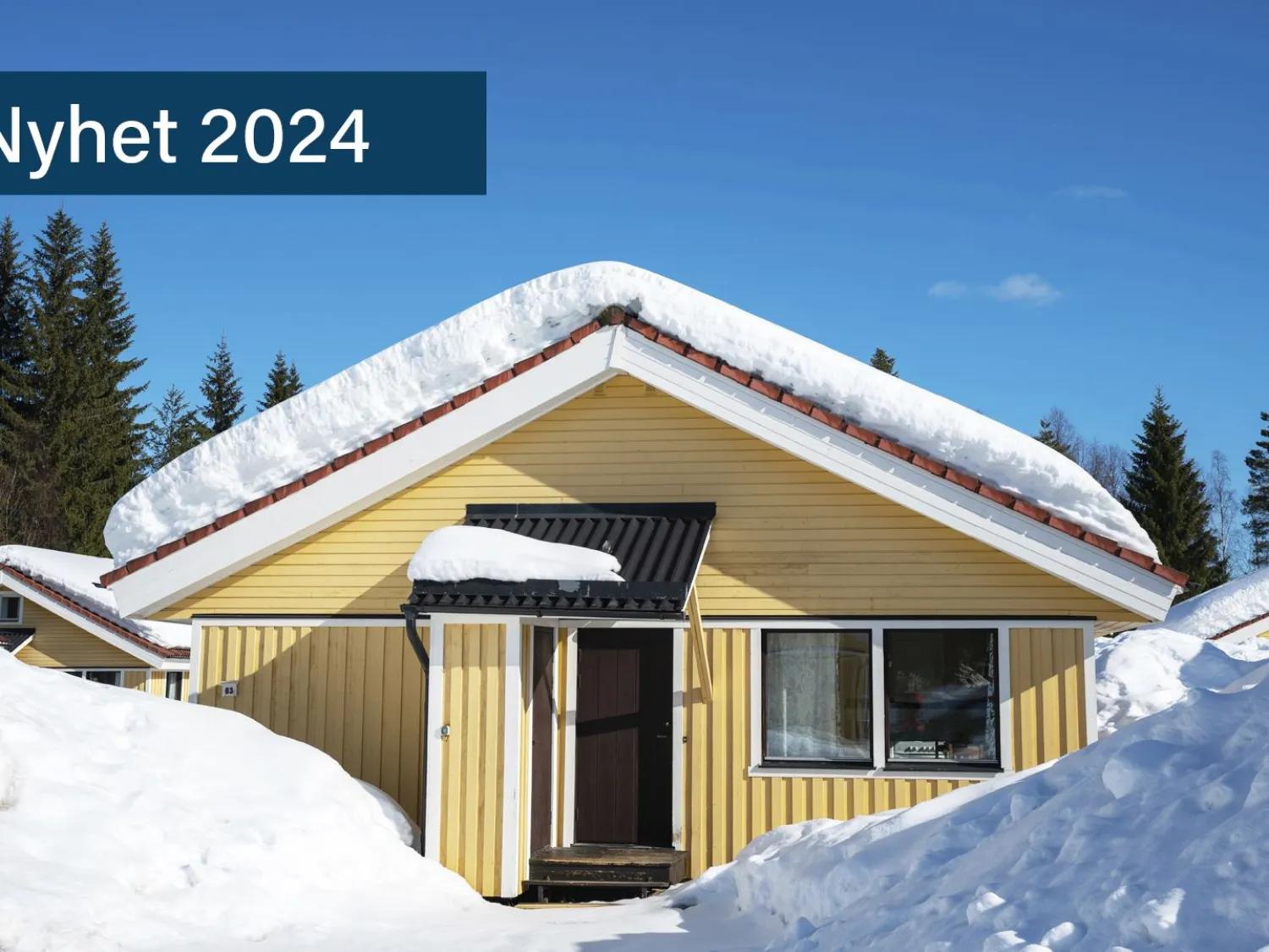 Exteriör av gul skidstuga Björnen, Hassela Ski Resort. Snö omger stugan och blå himmel ovan.