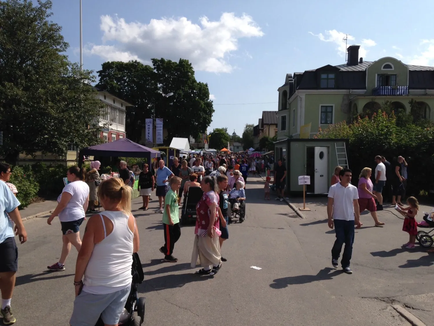Färgbild - utomhusbild med gatuvy. Bygata fylld med människor.