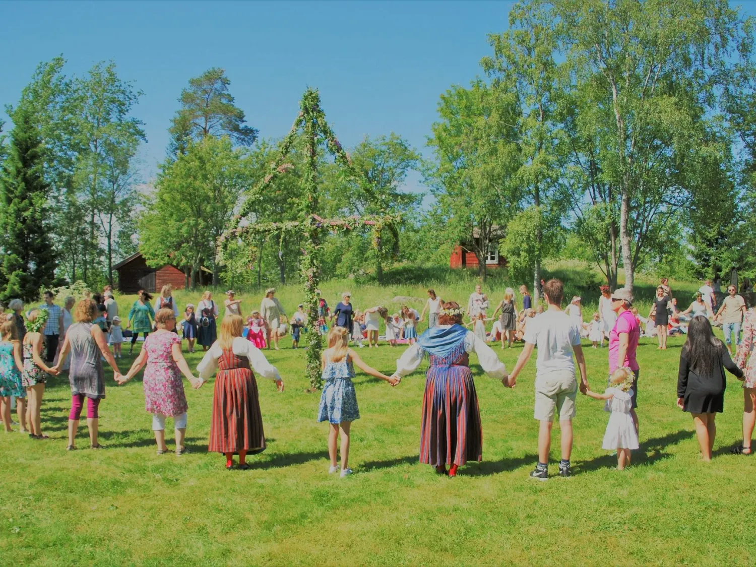 Färgbild - människor som dansar kring midsommarstång i grönskande sommar.