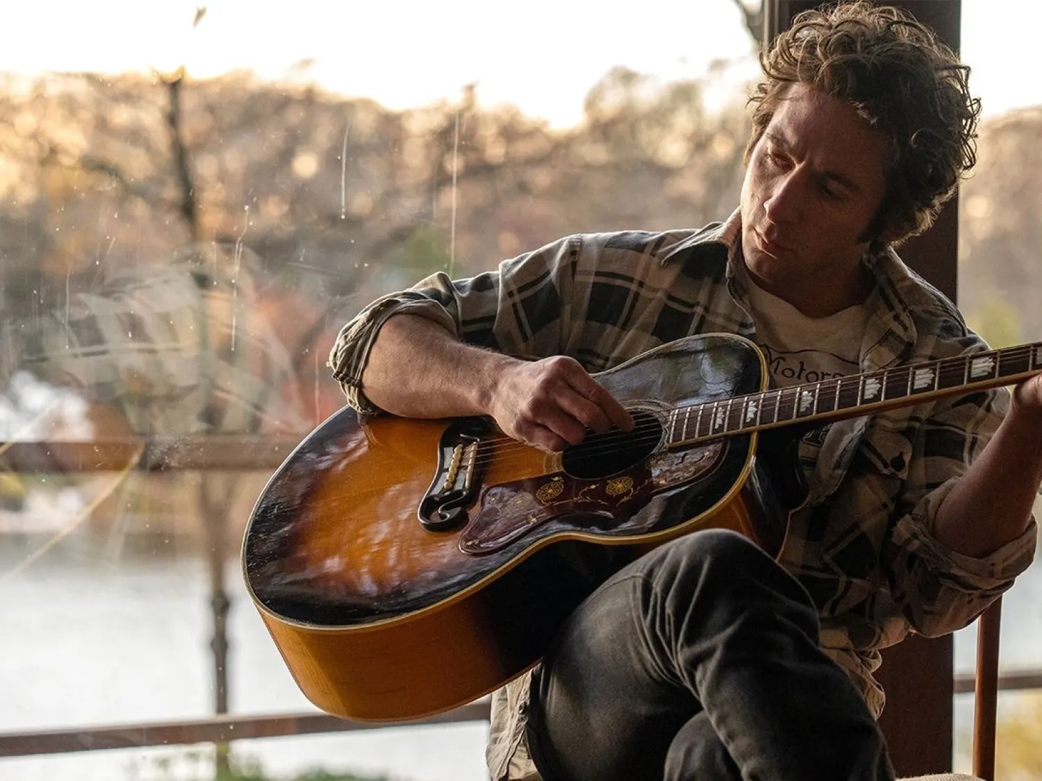 Färgbild - en man sittande i ett fönster och spelar gitarr.