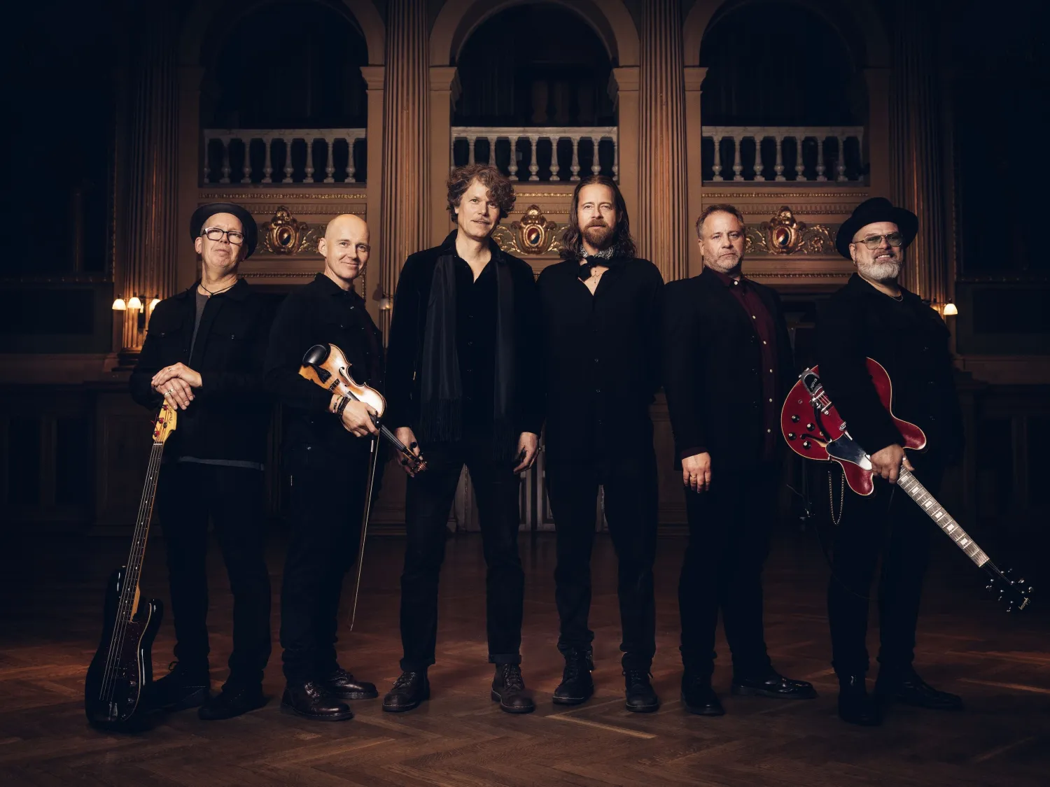 Färgbild - ett porträtt inomhus av en grupp manliga musiker i mörka kläder. Mörk inomhusmiljö.