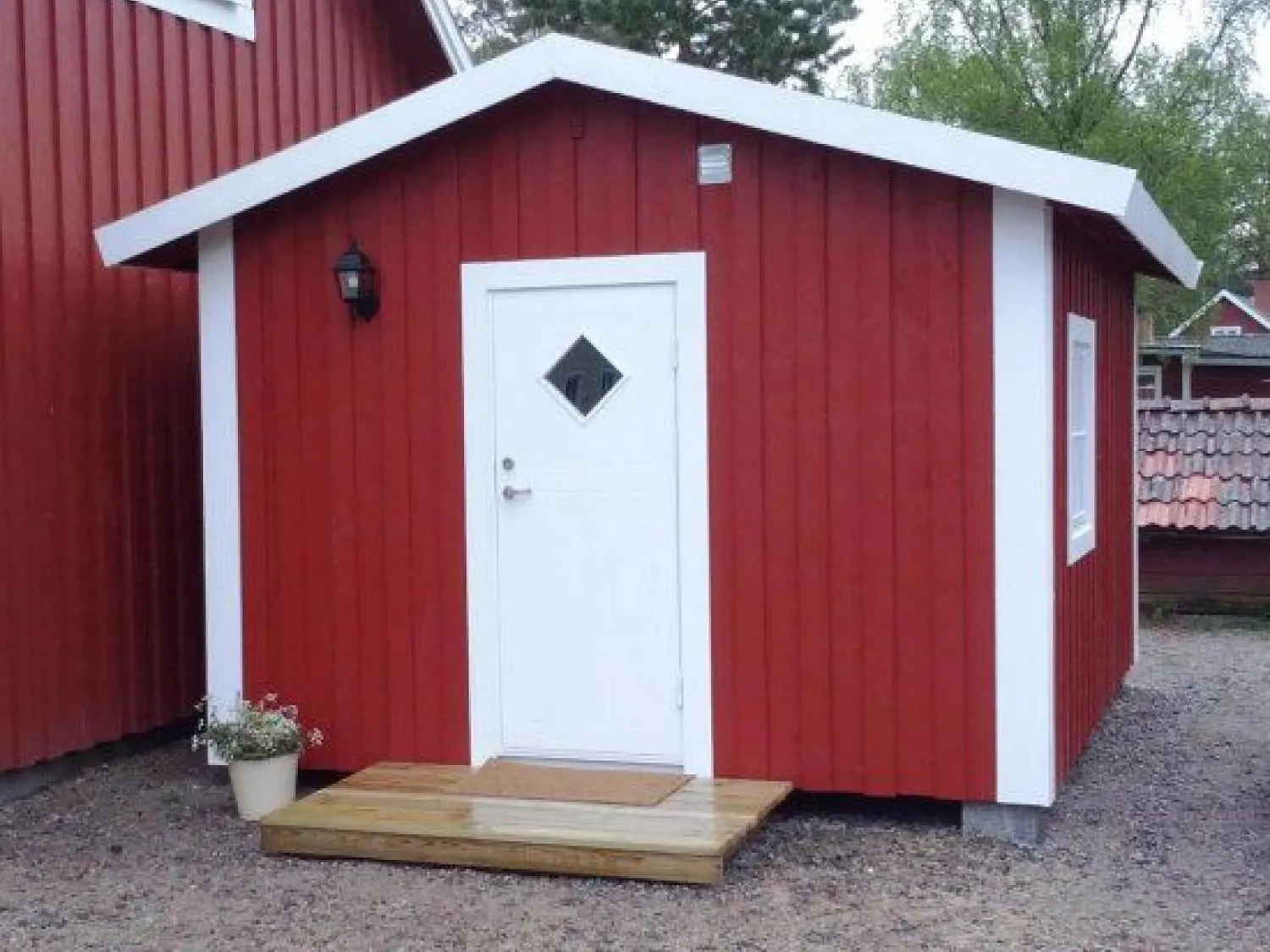 En röd liten trästuga med vit dörr och knutar