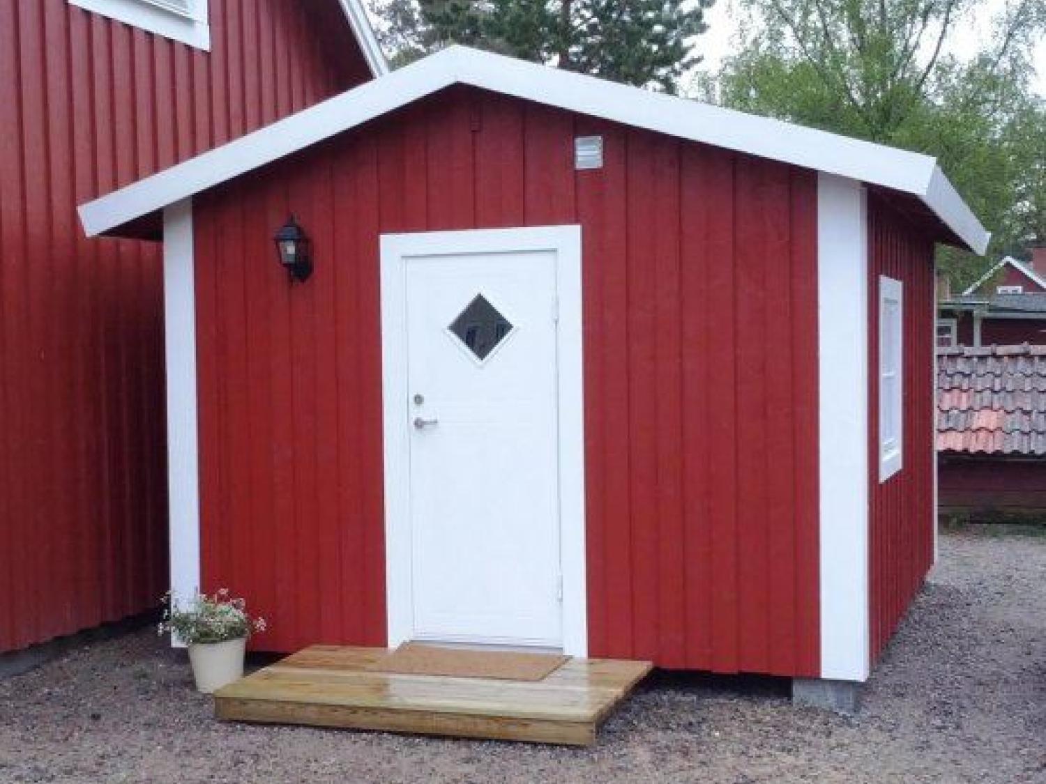 En röd liten trästuga med vit dörr och knutar