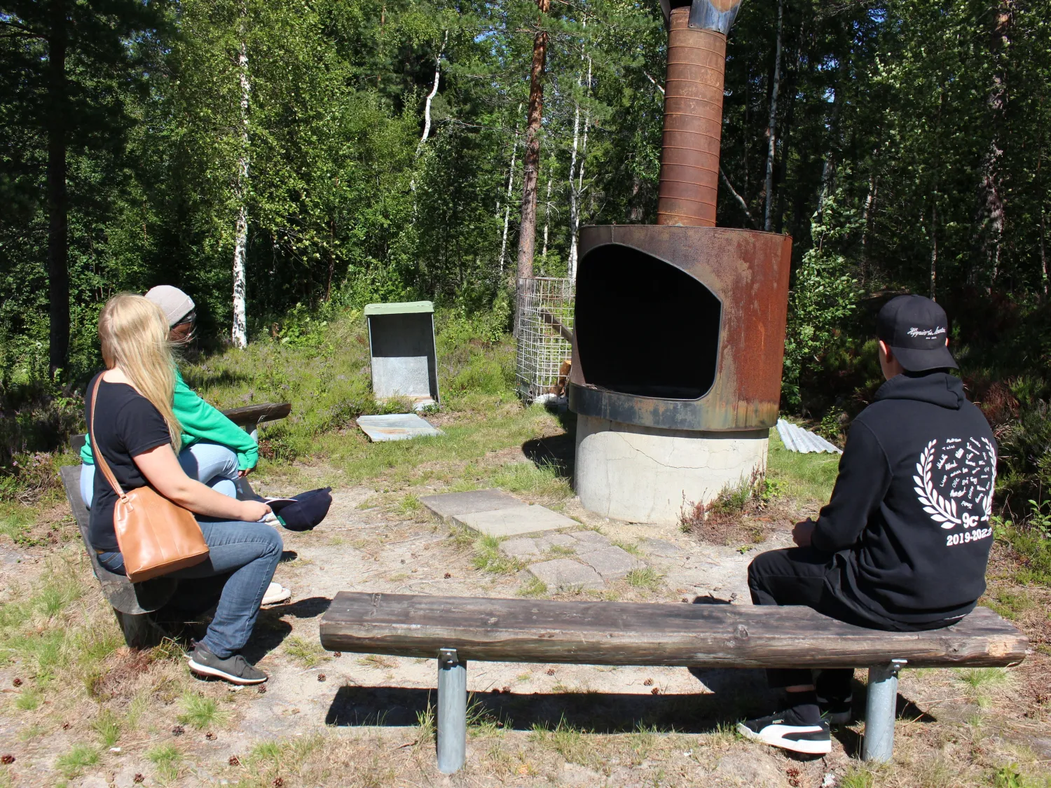 Tre personer sitter runt grillplats