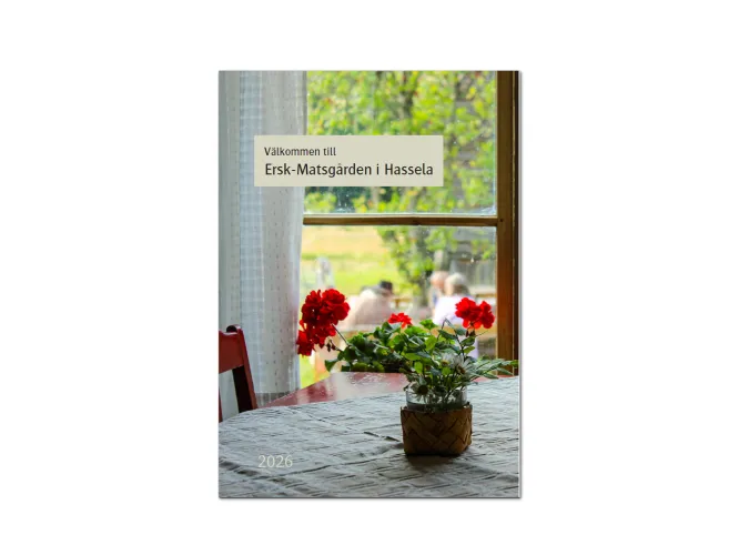 Färgbild - framsida av folder för Ersk.Matsgården 2026. Utsikt från en fönster på gården, med en blomma på ett bord i förgrunden