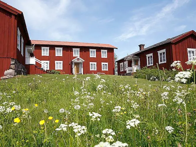 Länkad bild till ny webbplats i nytt fönster - Exteriör Bild på rödvita träbyggnader omgiven av grönska och blommor