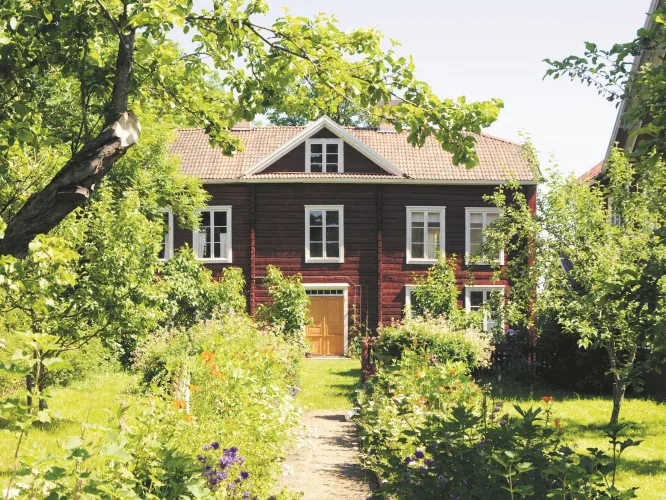 Färgbild - exteriör av världsarvsgård Erik-Anders. Rödvit träbyggnad i trädgårdsmiljö