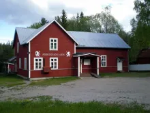 Årskogslokalen Årskogslokalen - exteriör, röd fasad och vita knutar, entredörr och brokvist.