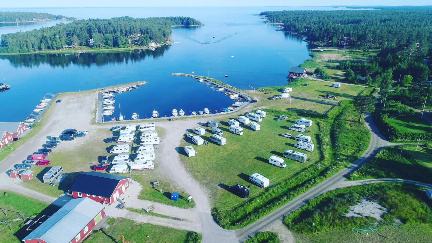 Färgbild - drönarvy över kustorten Mellanfjärden med hamninfart, camping med husbilar och havet i bakgrunden