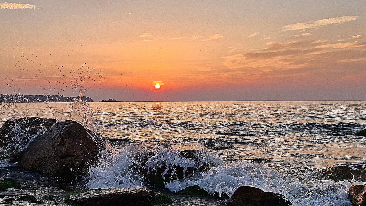 Färgbild - solnedgång vid havet med vågor som slår mot klipphällar