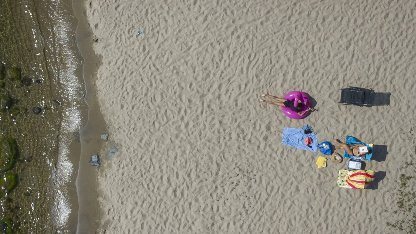 Färgbild - drönarbild över havsstrand med solbadande människor och vattenbryn till vänster i bild...