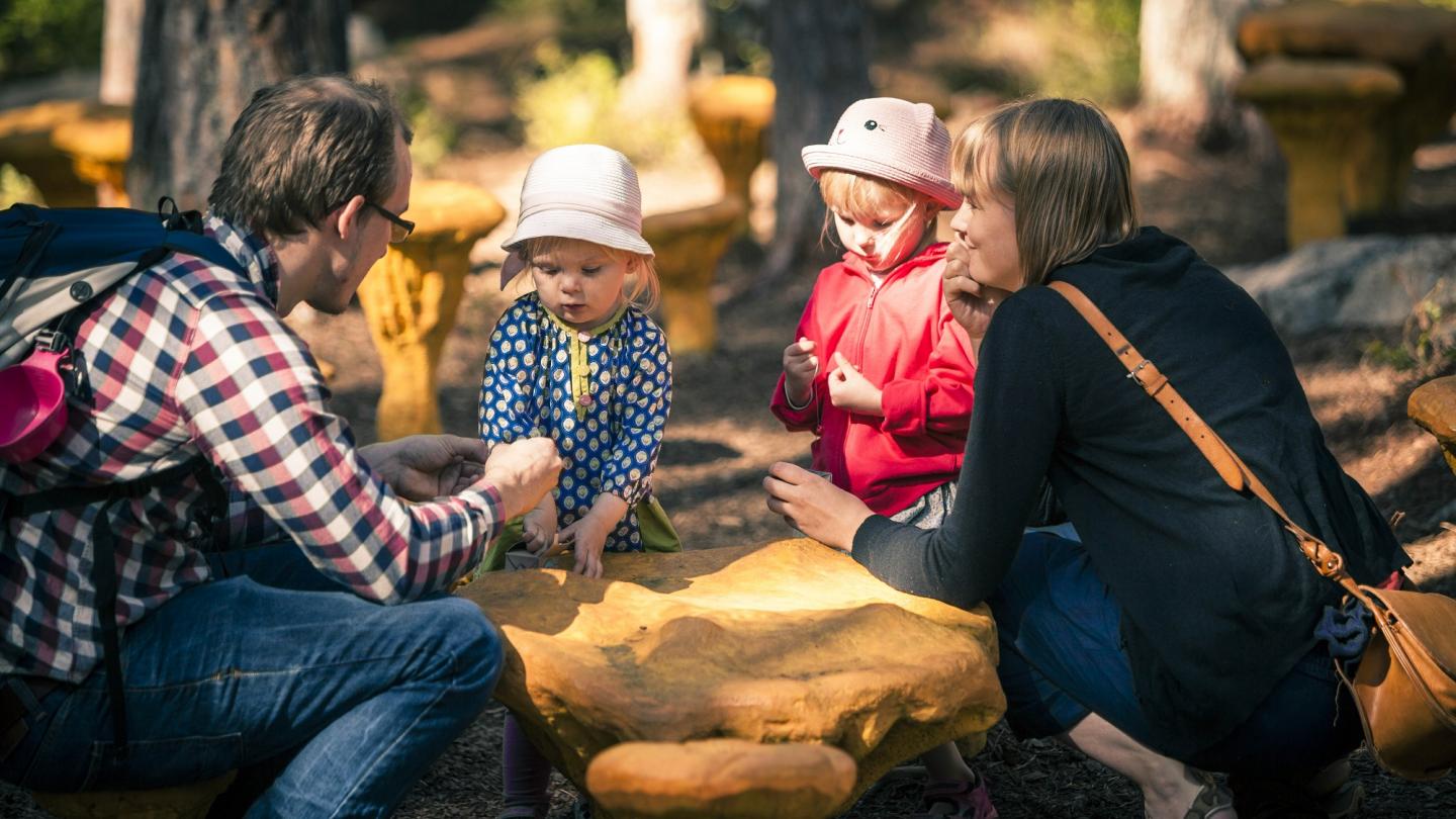 Familj som sitter på huk i Trolska Skogen runt en stor kantarell.