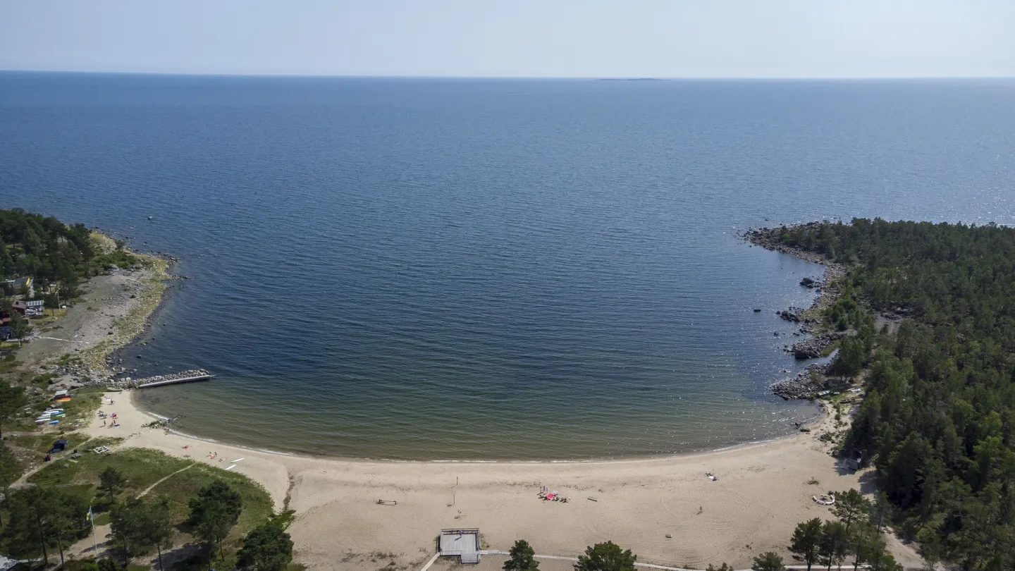 Färgbild - drönarbild över havsbukt med badstrand och havshorisont.