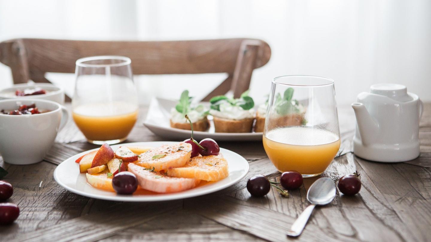 Frukost på bord med juice i glad, kaffekopp, frukt på fat och bröd.