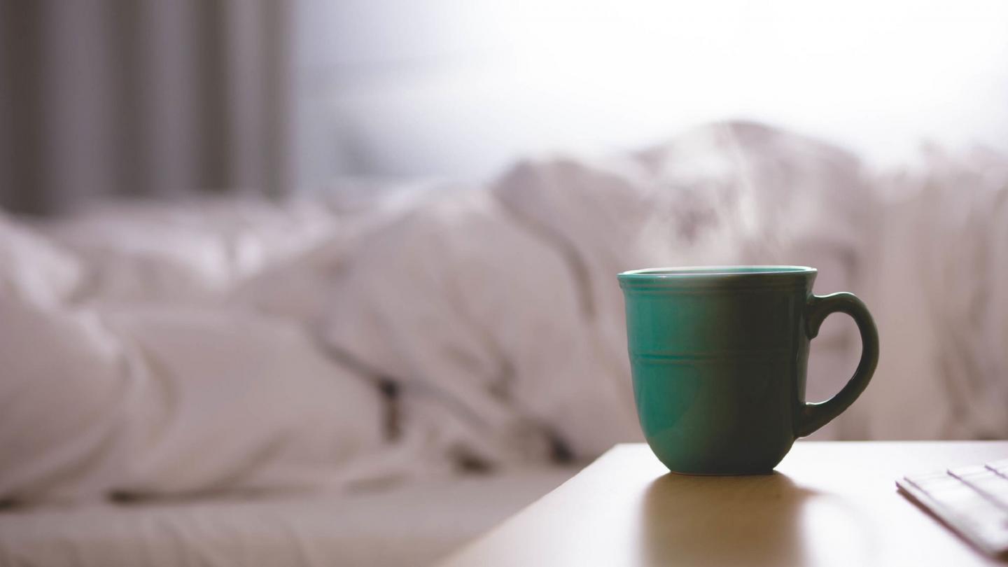 Kaffekopp på sängbord vid säng.
