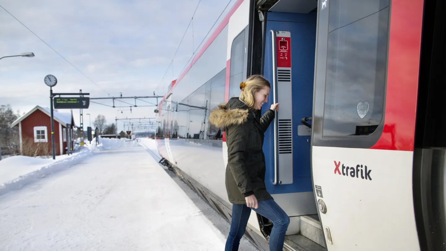 Färgbild - en kvinna som kliver på ett tåg från perrong. X-trafik Gnarp.