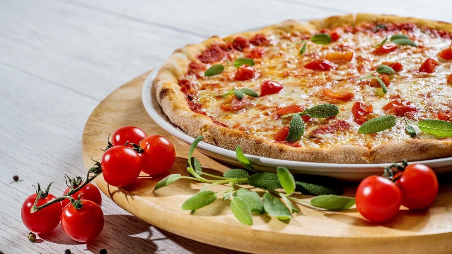 Pizza på tallrik med tomater och krydda bredvid.