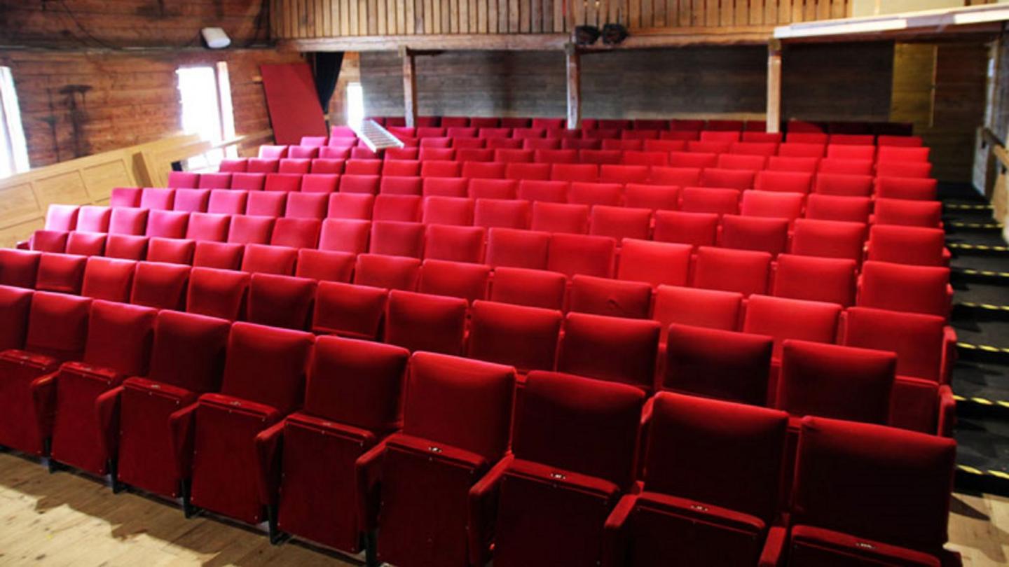 Rader med röda stolar i teatersalong.