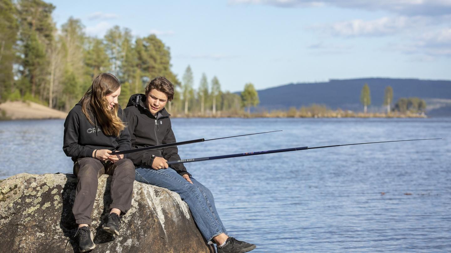 Färgbild - ungdomar sittande vid sjö och fiskar med metspö.